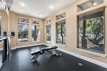 A gym room with a bench, weights, and windows.